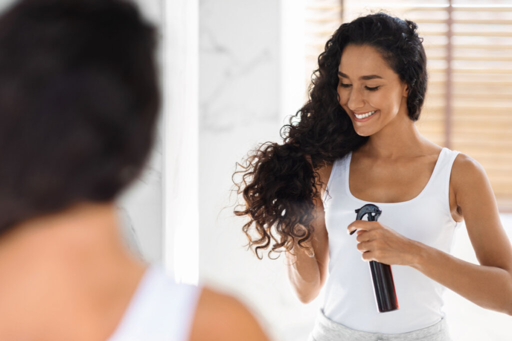 Mulher no espelho aplicando produto em spray no cabelo
