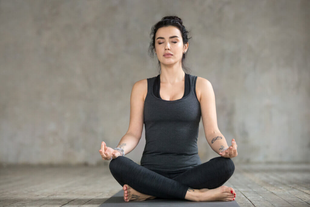 Mulher sentada no chão de pernas cruzadas praticando respiração na ioga