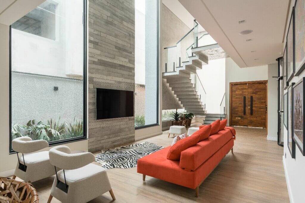 Sala de estar com sofá laranja, tapete, televisão e parede com revestimento em cimento