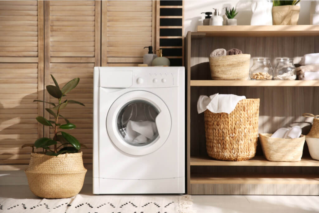 Interior de uma lavandeira com cestos e um secadora com roupas dentro e um vaso de planta ao lado