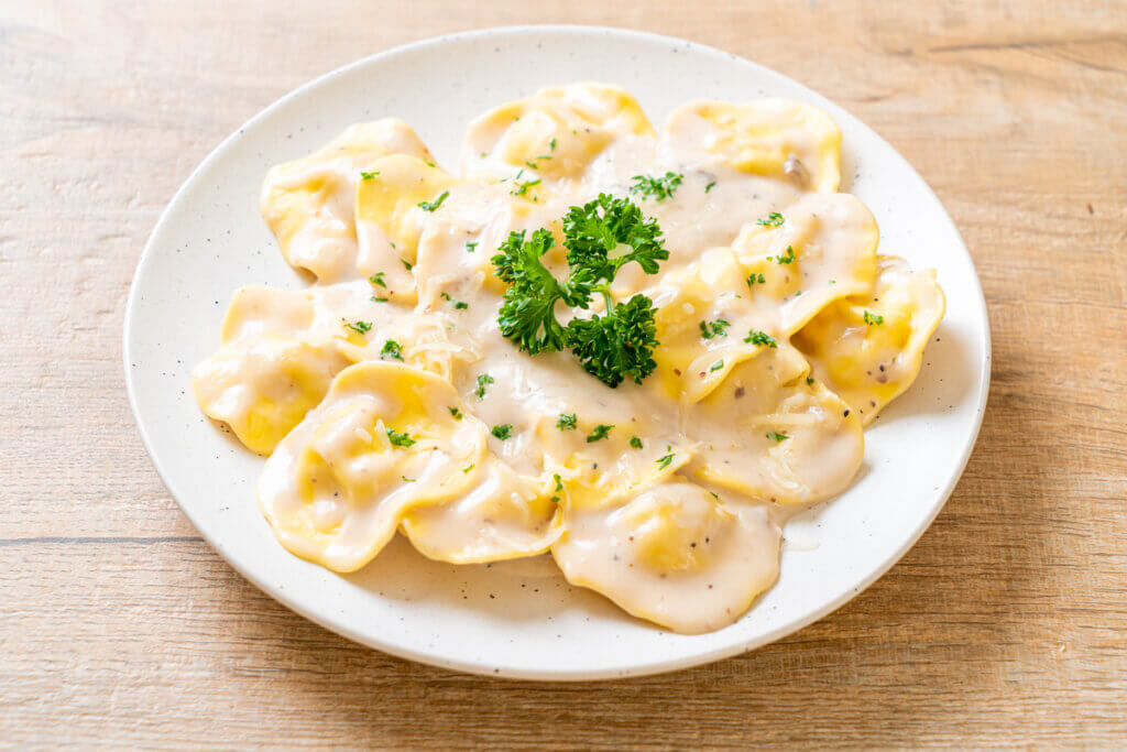 Ravioli com molho branco, polvilhado com salsa picada em um prato branco