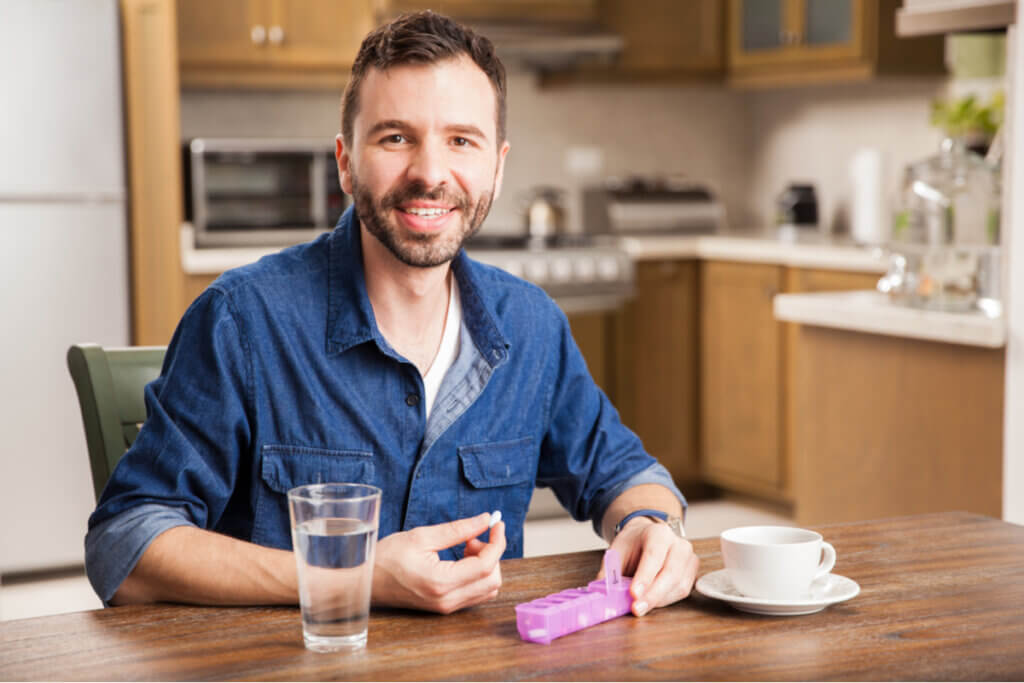 Homem sorrindo segurando recipiente com remédios
