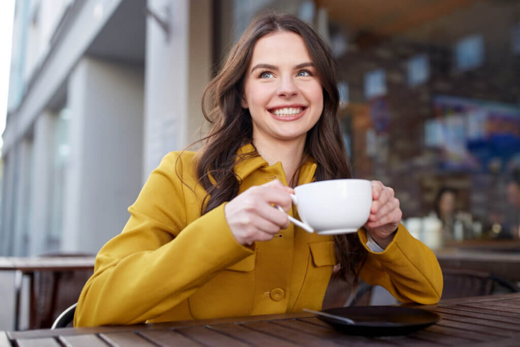 Mulher sentada sorrindo segurando uma xícara
