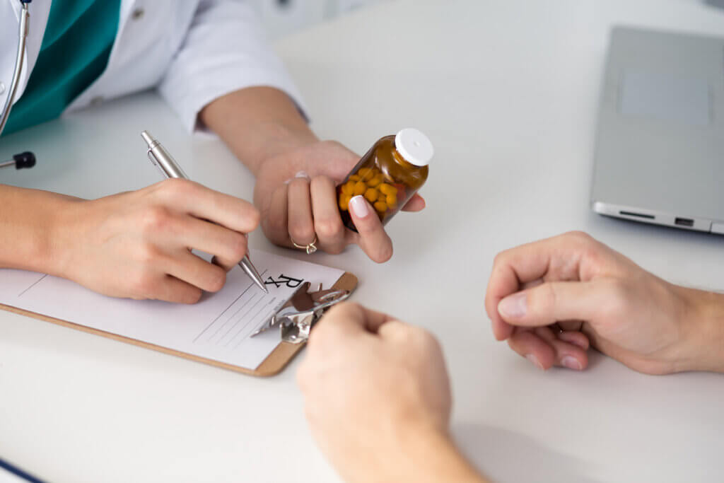 Médico receitando comprimido para paciente com uma caneta na mão e prancheta na mesa