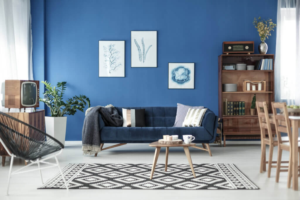 Sala de estar com parede azul, tapete geométrico, sofá, armário de madeira, mesa de centro e quadros na parede