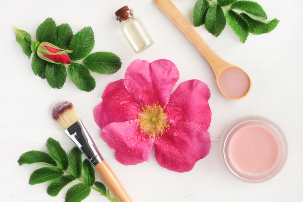 Mesa branca com flores de cor rosa, pincel de maquiagem e um pote com creme rosa dentro de um pote para beleza