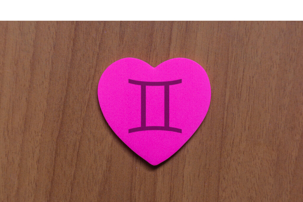 Coração rosa de papel com o símbolo do signo de Gêmeos em cima de uma mesa de madeira marrom
