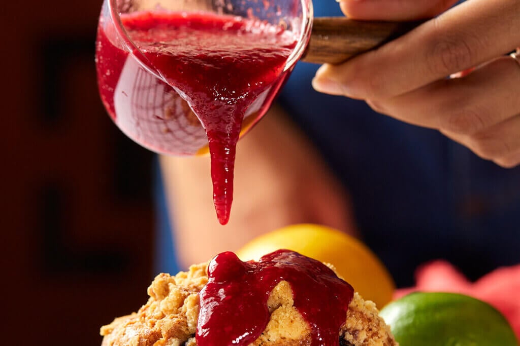 Geleia de frutas vermelhas em recipiente sendo despejada sobre bolo