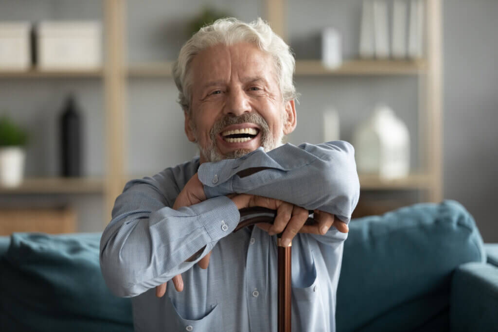 Homem idoso sentado em sofá com os braços e rosto apoiado em bengala