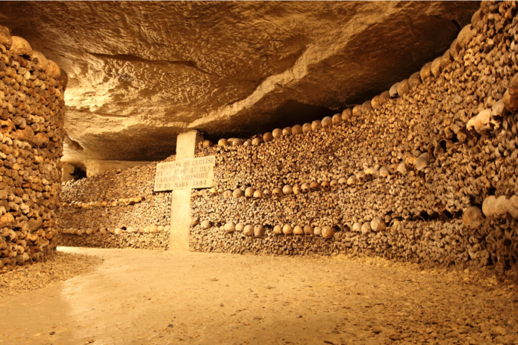 Vista de dentro das catacumbas de Paris com ossos e uma cruz na parede