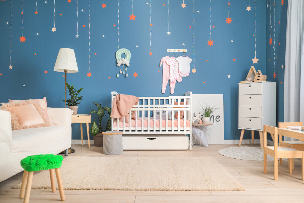 Quarto de bebê com parede azul, berço, cômoda e luminária