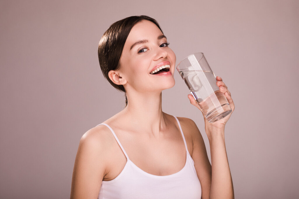 Mulher sorrindo e segurando um copo d'água cheio na mão