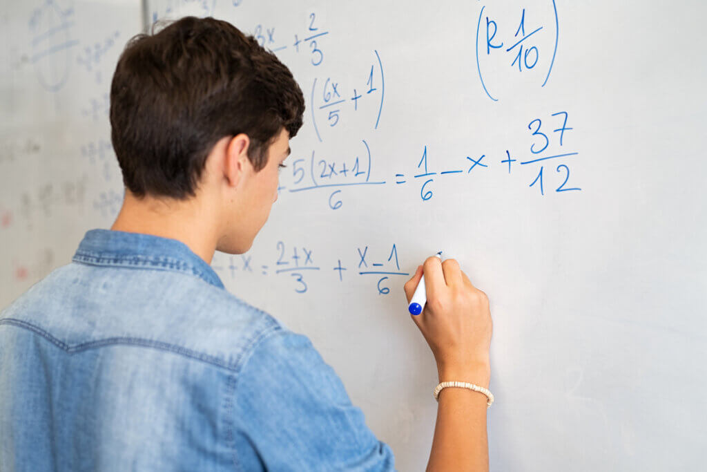 Jovem rapaz escrevendo no quadro branco equações matemáticas com uma caneta azul