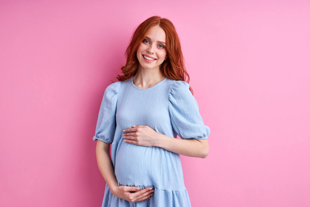 Mulher gravida de vestido azul, sorrindo e segurando a barriga