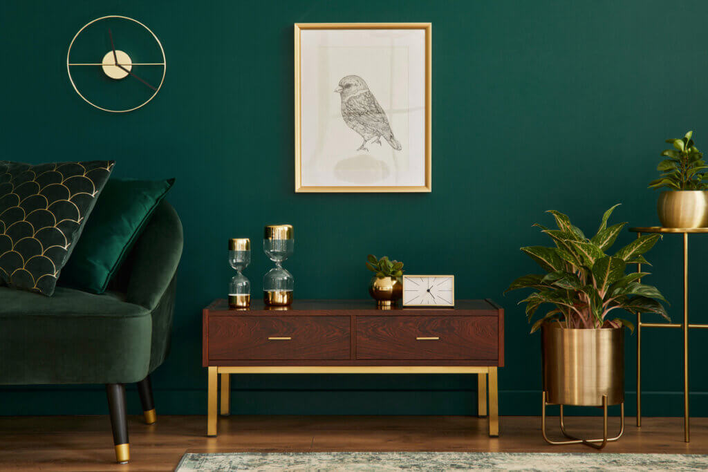 Cantinho com mesa de madeira com objetos decorativos em cima, vasos de planta, sofá verde com almofadas e quadro