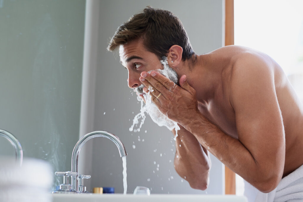 Homem lavando a barba em frente a um espelho