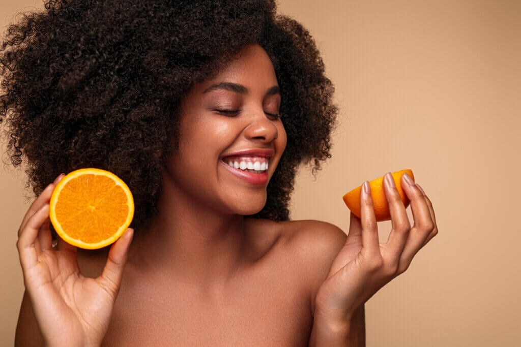 Mulher sorrindo e segurando metades de laranja com as mãos