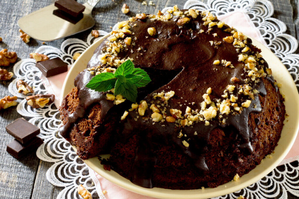 Bolo de chocolate com cobertura de brigadeiro e pedaços de nozes em cima de um prato branco 