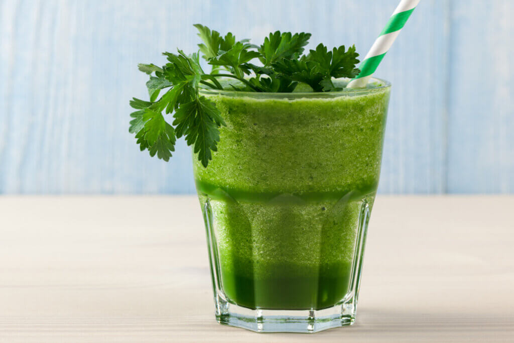 Copo transparente com suco verde, folhas de salsa e canudo