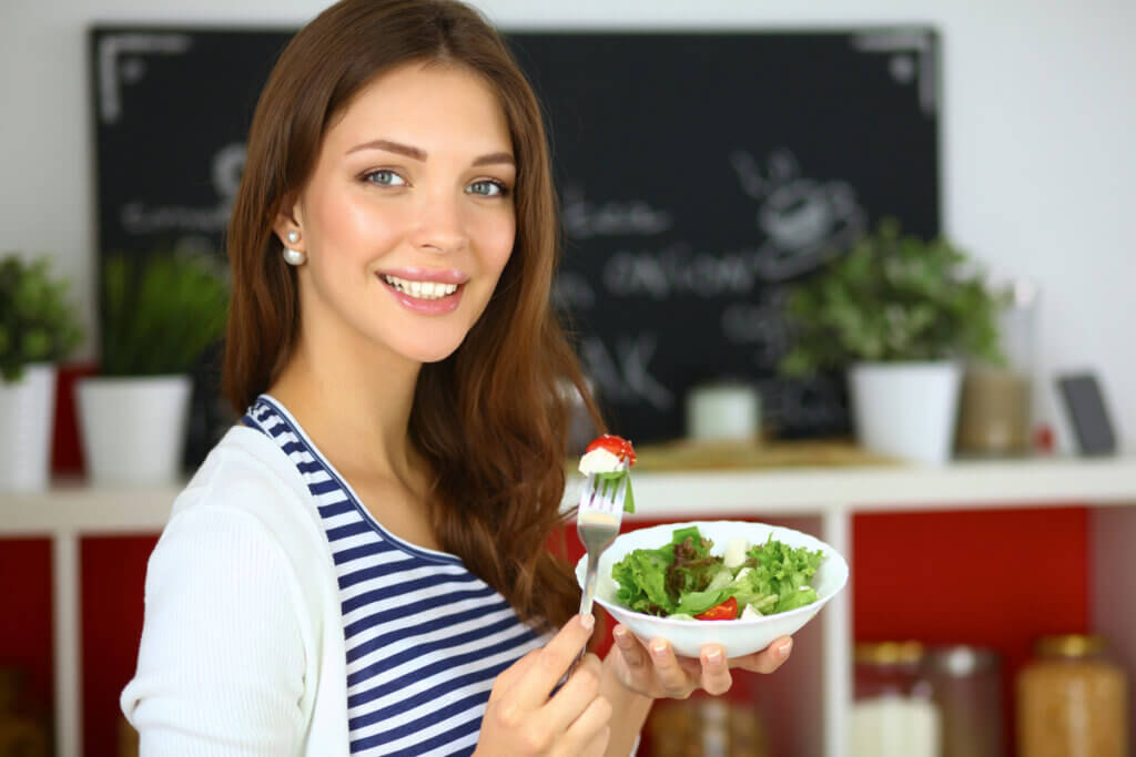 Mulher sorrindo e segurando um pote branco com salada dentro