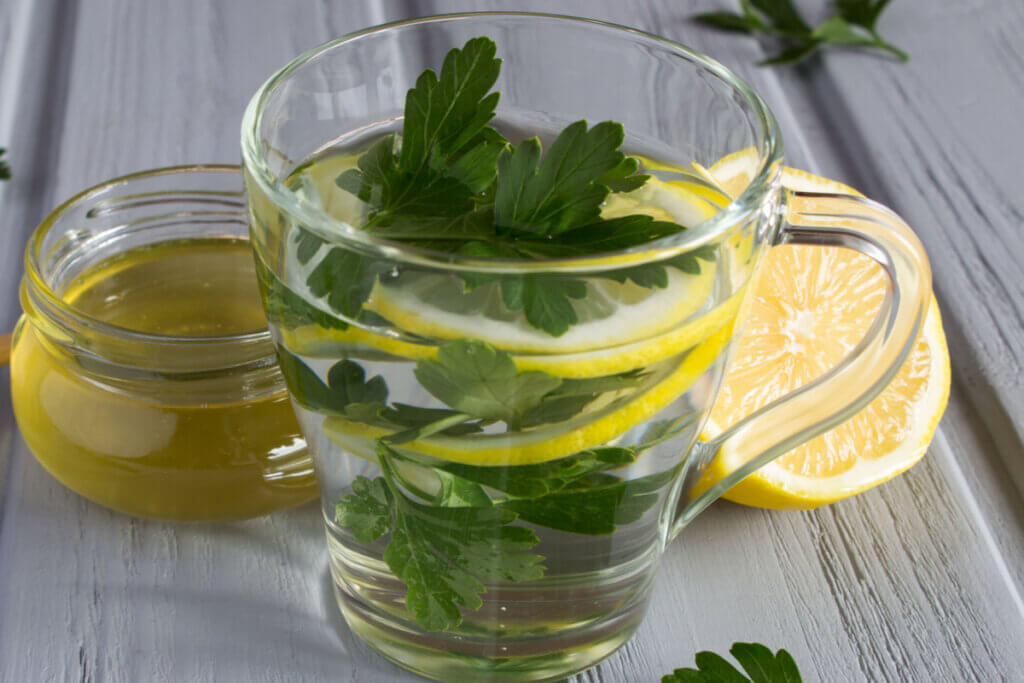 Recipiente transparente com chá, folhas de salsa e pedaços de limão 