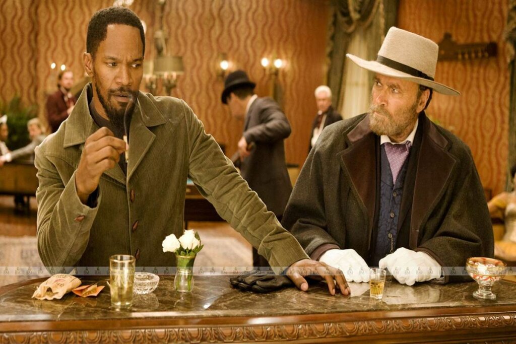 Jamie Foxx e Christoph Waltz na cena do filme Django Livre sentados em uma mesa