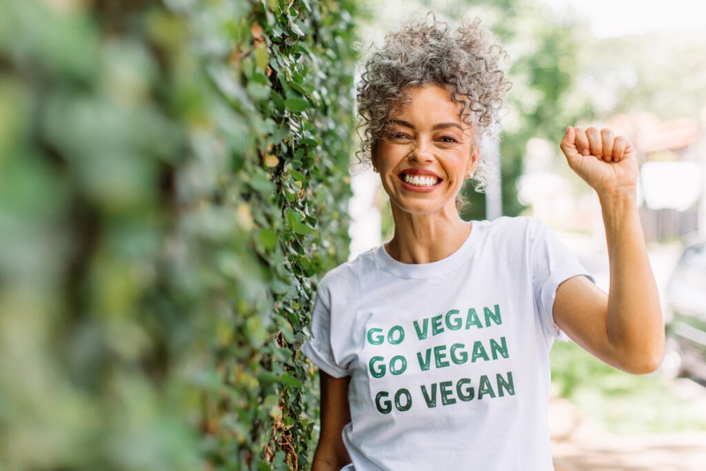 Mulher negra com cabelos cacheados presos e com camiseta branca com a frase Go Vegan