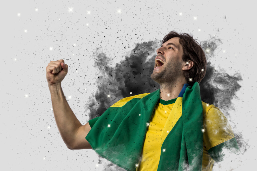 Homem jovem com camisa amarela e com a bandeira do Brasil nos ombros.