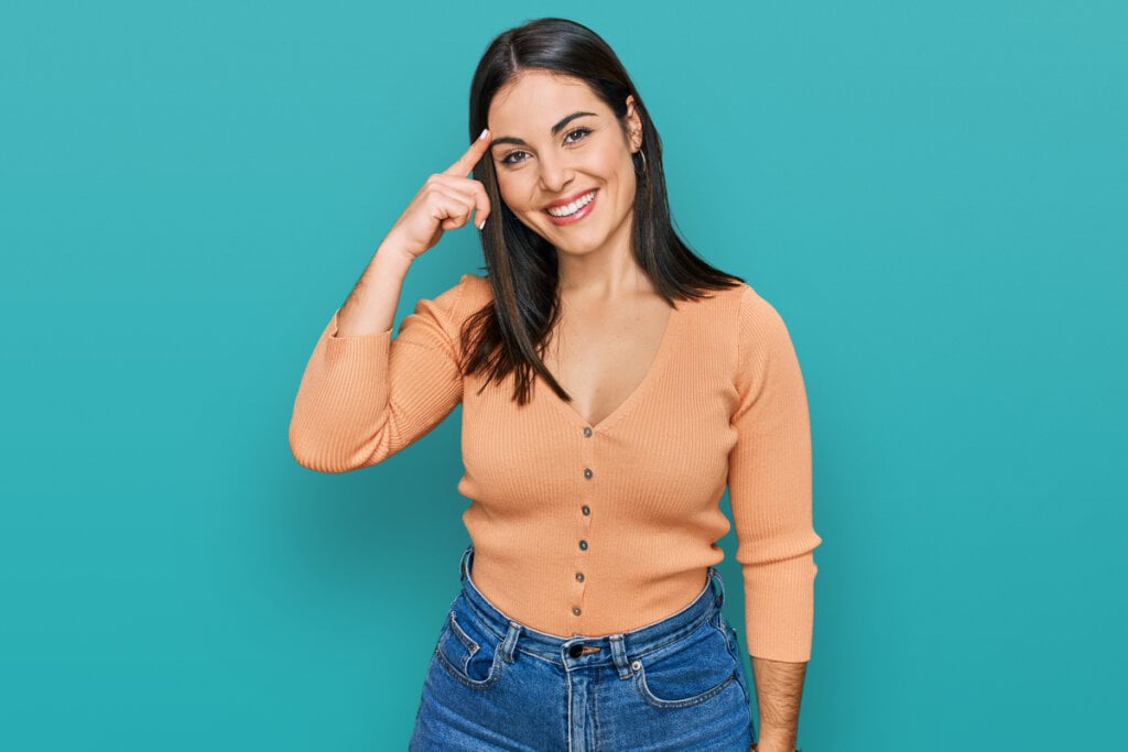 Mulher de blusa laranja com as mãos na cabeça sorrindo