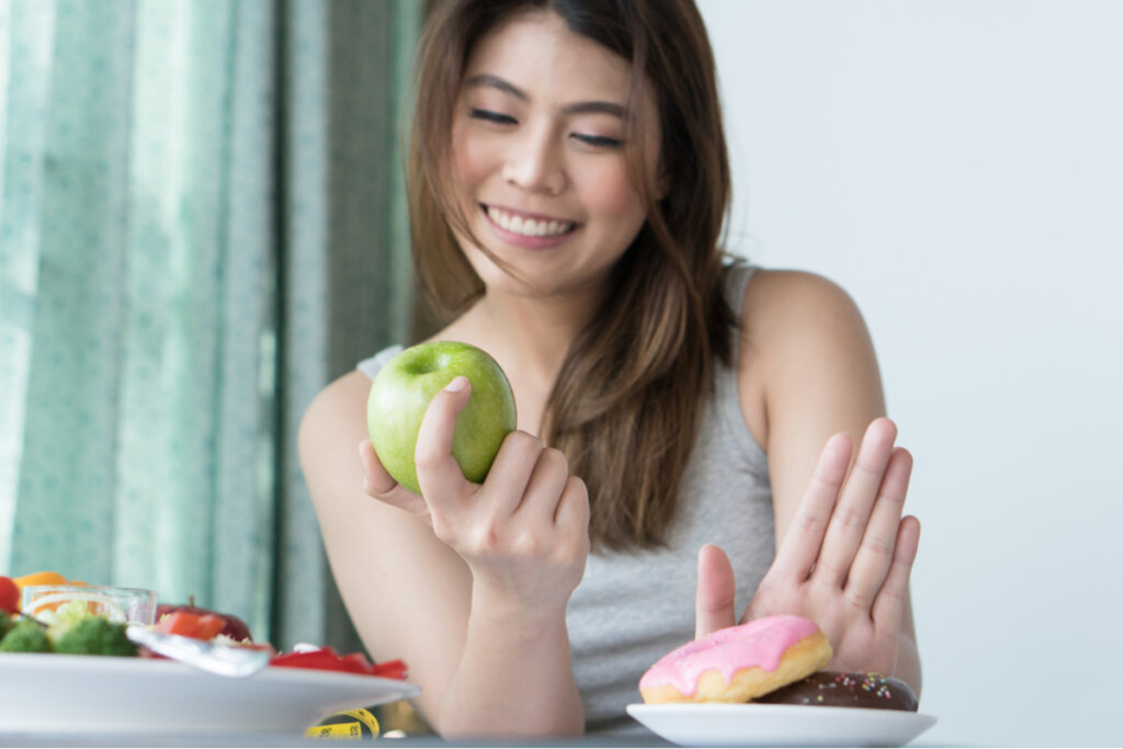 Mulher sorrindo, segurando uma maçã e dispensando um donut