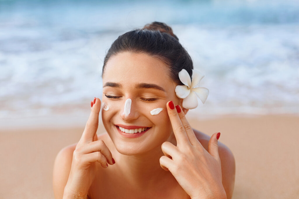 Mulher sorrindo passando protetor no rosto na praia