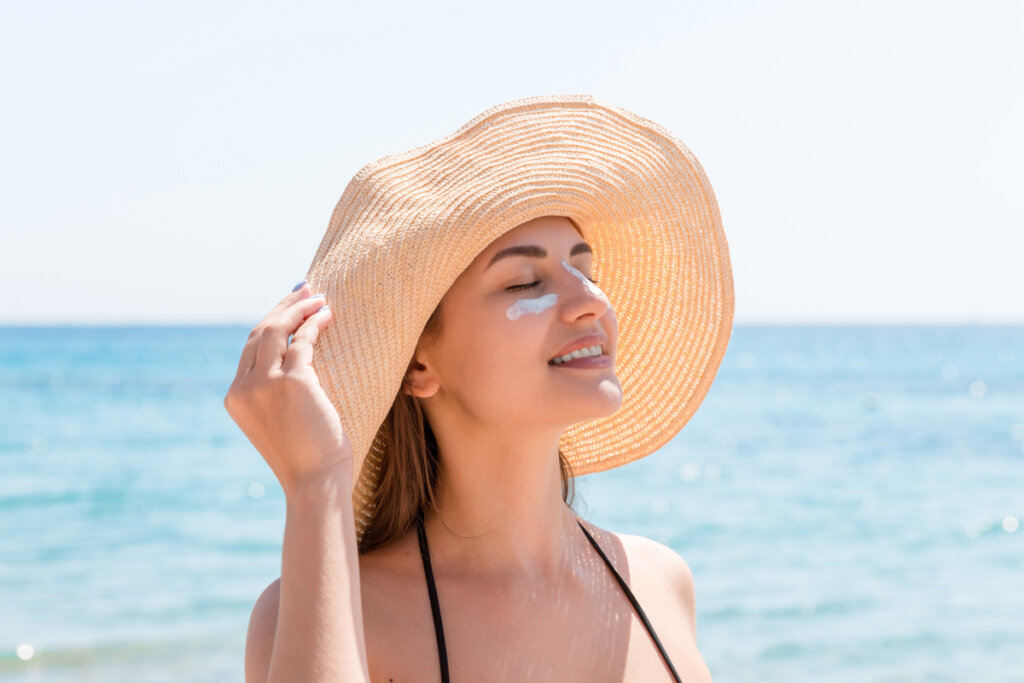 Mulher na praia usando chapéu e com protetor solar no rosto