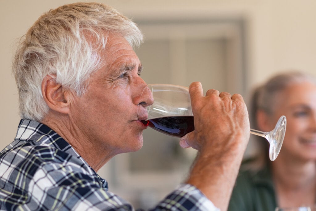 Homem de meia idade tomando vinho em uma taça de vidro