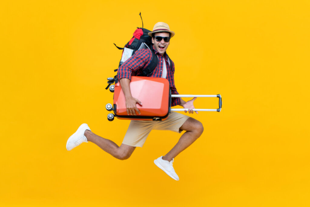 Homem feliz, pulando e segurando malas de viagem