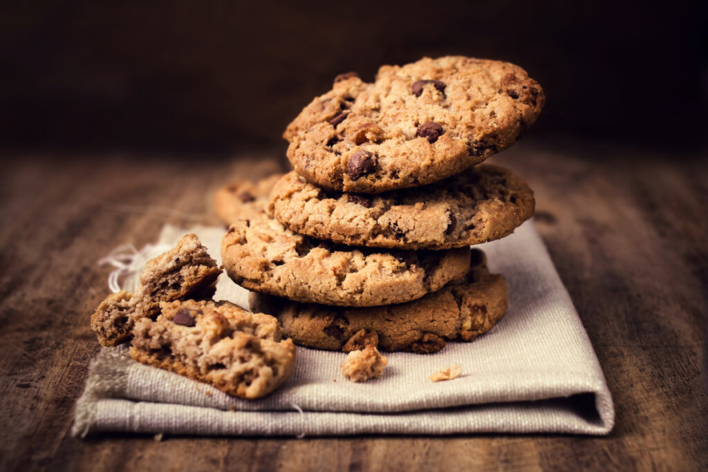 Cookies com gotas de chocolate em cima de um pano e em cima da mesa de madeira