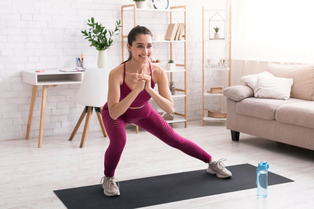 Mulher com roupa de ginástica em sala de estar praticando atividade física
