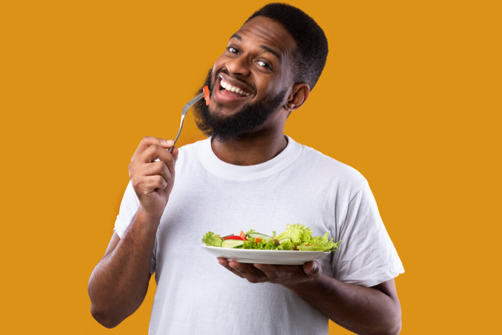 Homem sorrindo segundo um prato com salada e garfo com um pedaço de tomate