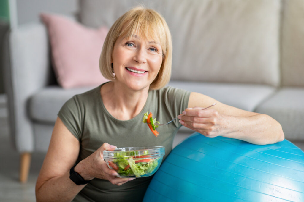 Mulher sorrindo segurando um recipiente e garfo com salada