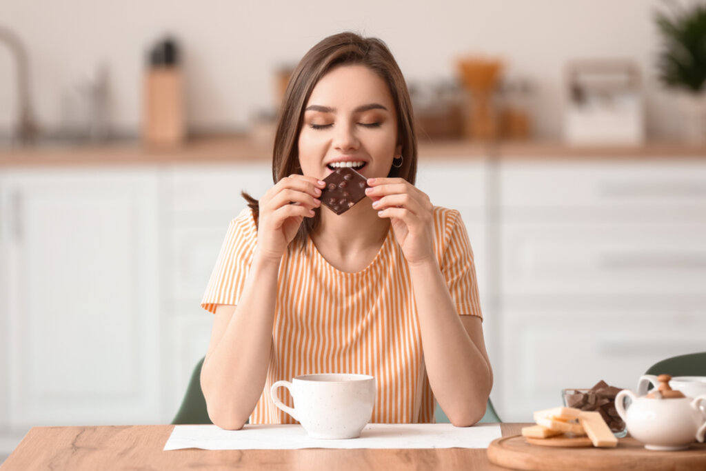 Mulher sentada de olhos fechados comendo chocolate