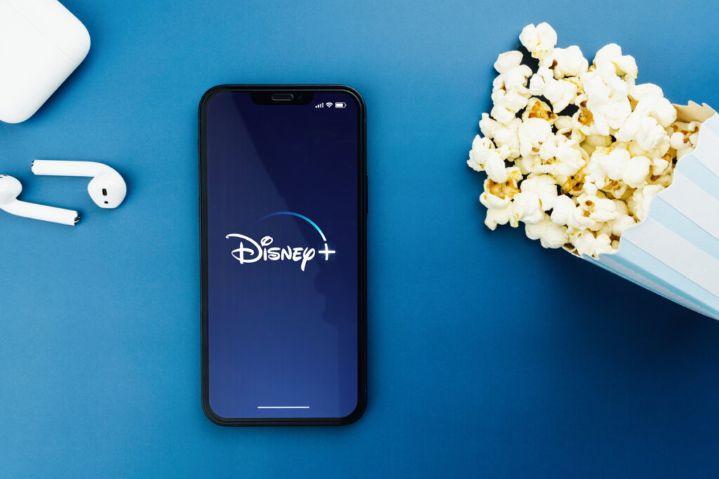 Celular com logo do Disney+, fones de ouvido sem fio e balde de pipoca