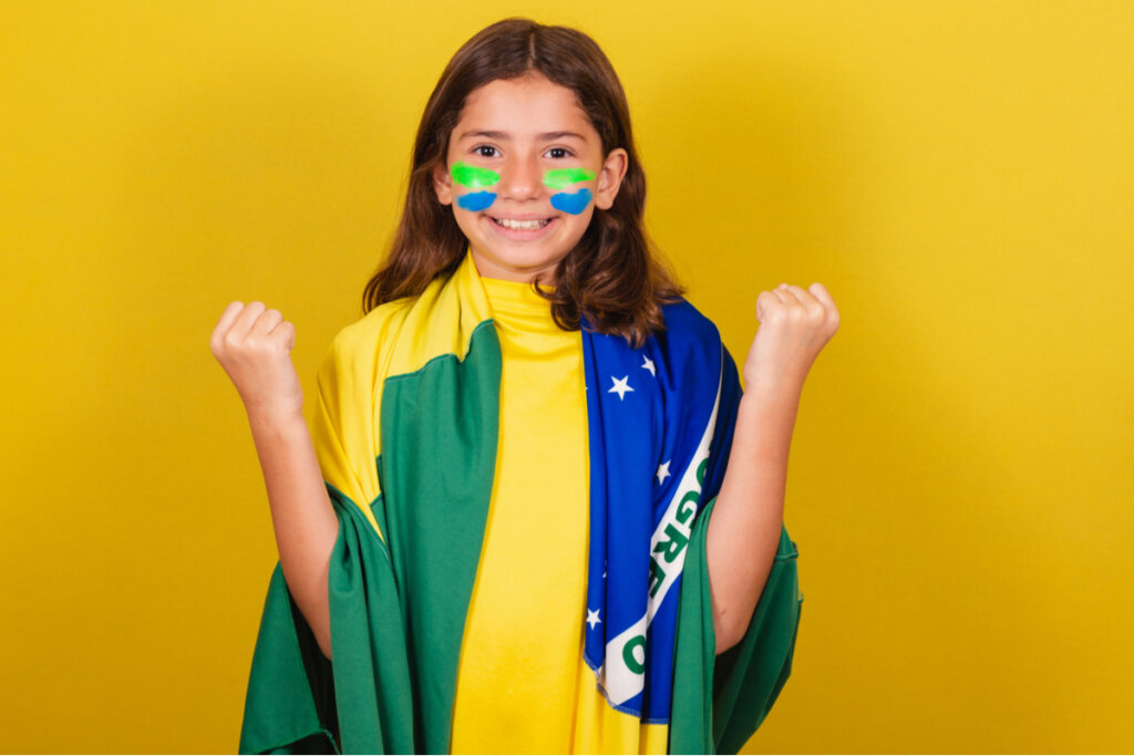Menina com bandeira do Brasil e rosto pintado de verde, amarelo e azul no fundo amarelo