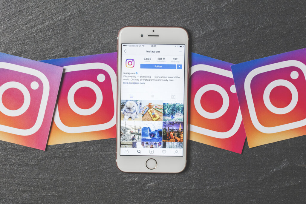 Celular com feed do Instagram na tela e logos do app em volta