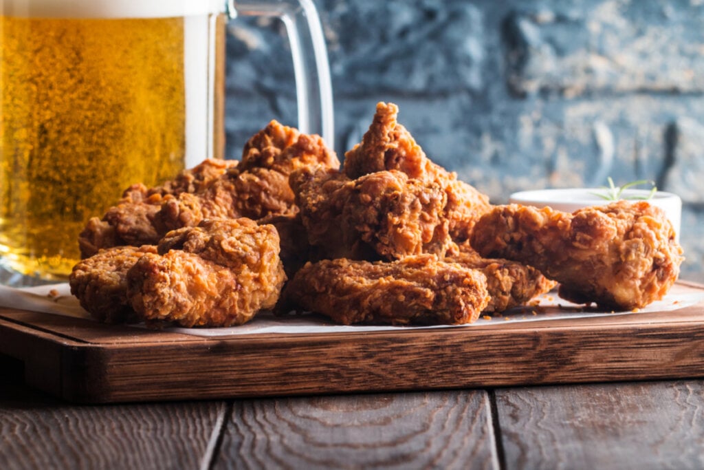 Frango empanado em cima de uma tábua de madeira com copo de cerveja de fundo