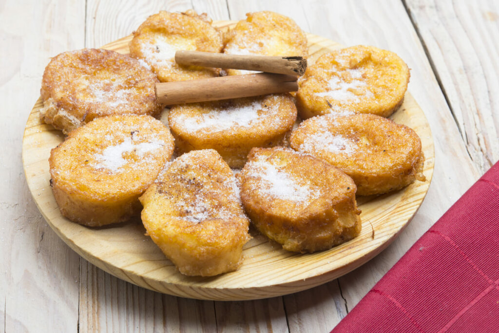 Rabanadas empilhadas em uma tábua de madeira com canela em pau