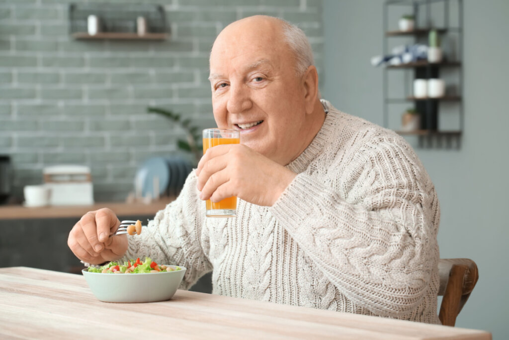 Homem de meia idade sentada comendo e tomando suco 