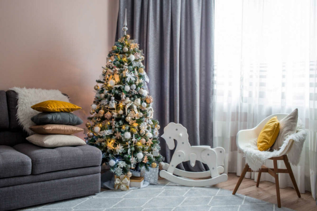 Sala de estar com sofá, árvore de Natal enfeitada, cavalinho de madeira e cadeira branca