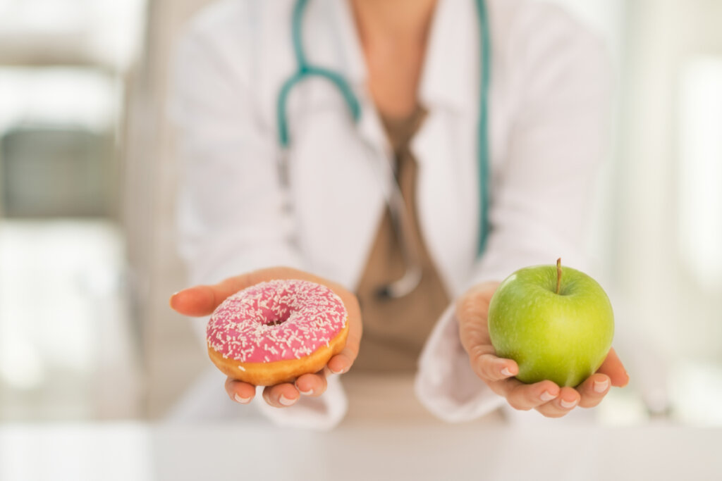 Médica segurando um donut com cobertura rosa em uma mão e na outra uma maçã verde 