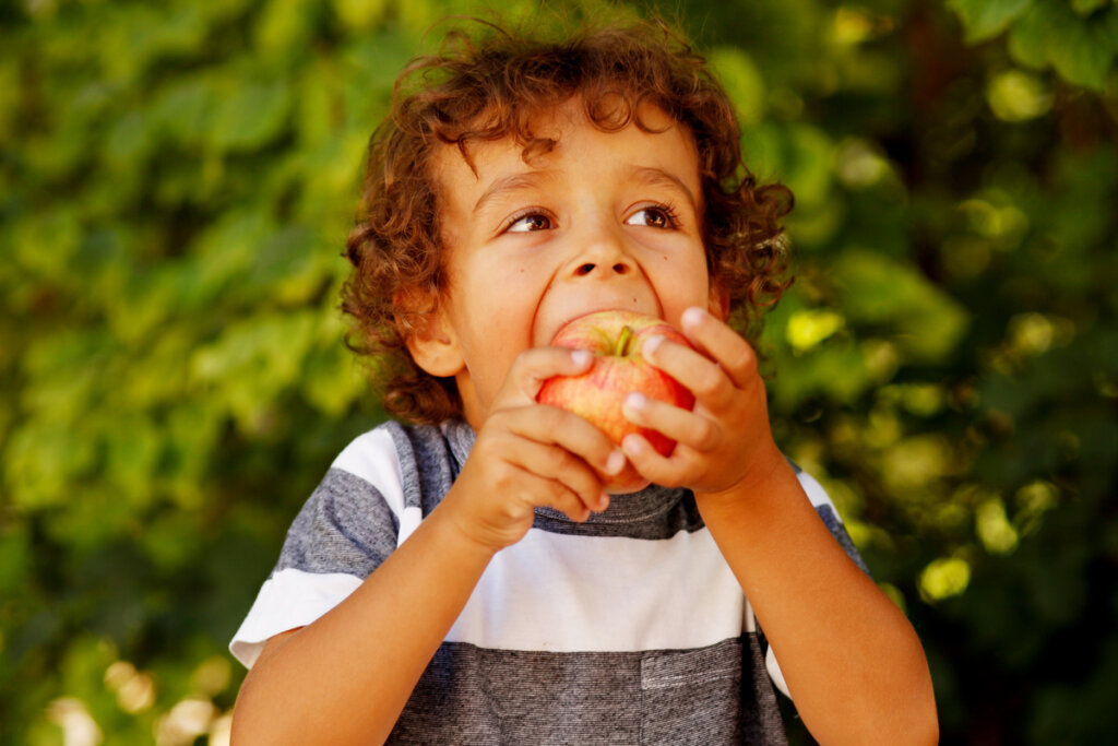 Menino de camiseta listrada e cabelo cacheado comendo maçã