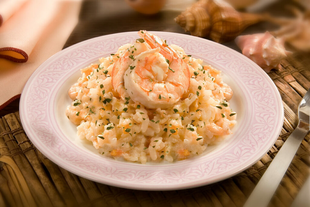 Risoto de camarão dentro do prato branco em cima da mesa de madeira