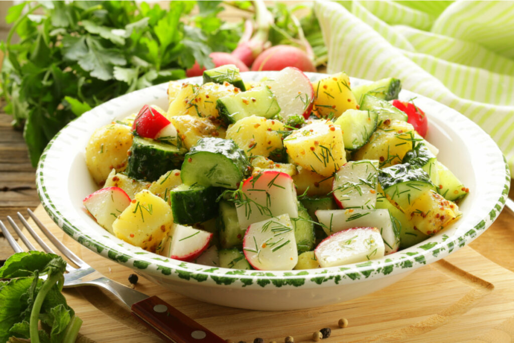 Salada com batatas, pepino e rabanete dentro do bowl branco e folhas verdes ao fundo